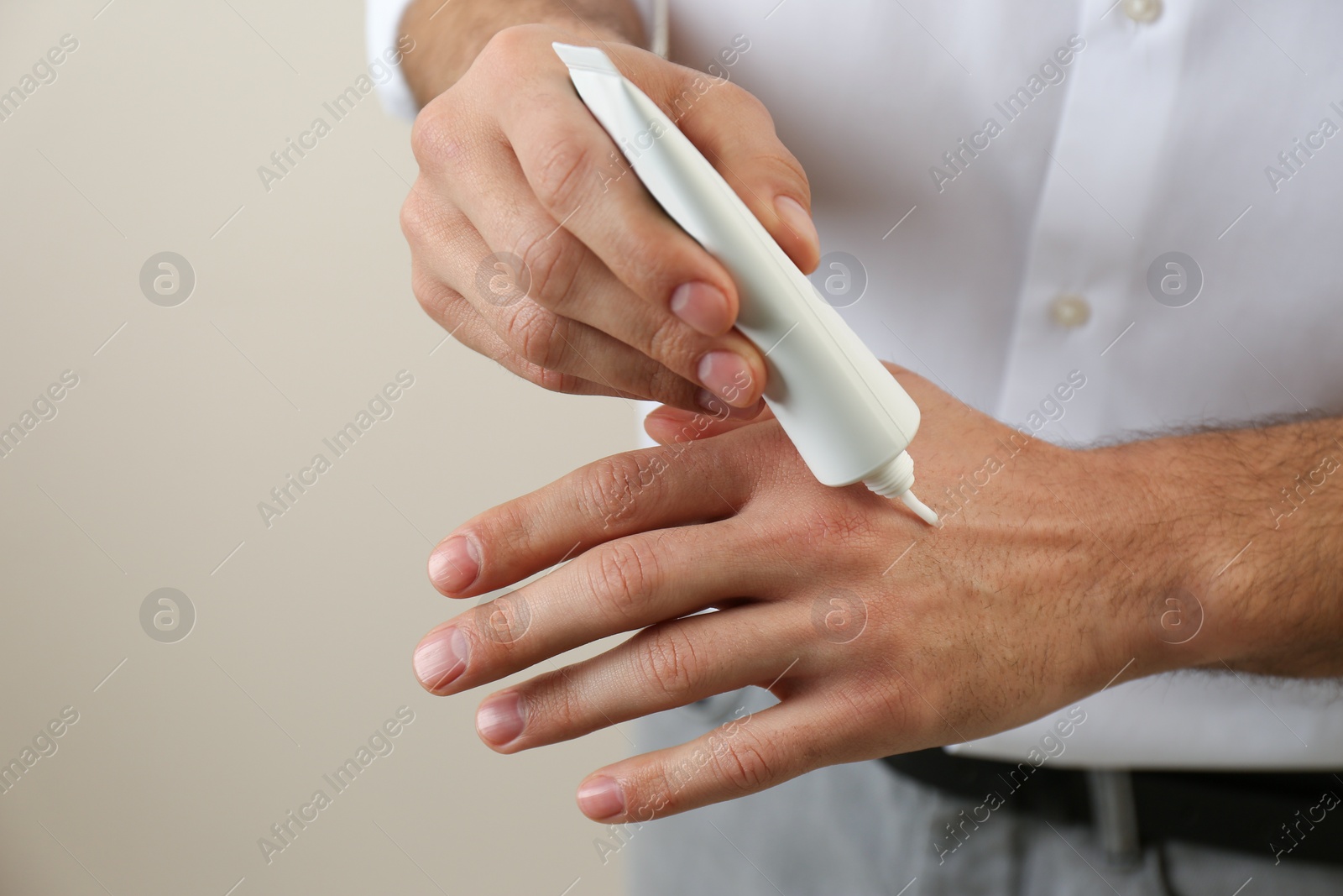 Photo of Man applying cream from tube onto hand on beige background, closeup