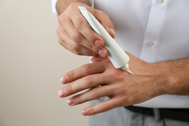 Photo of Man applying cream from tube onto hand on beige background, closeup