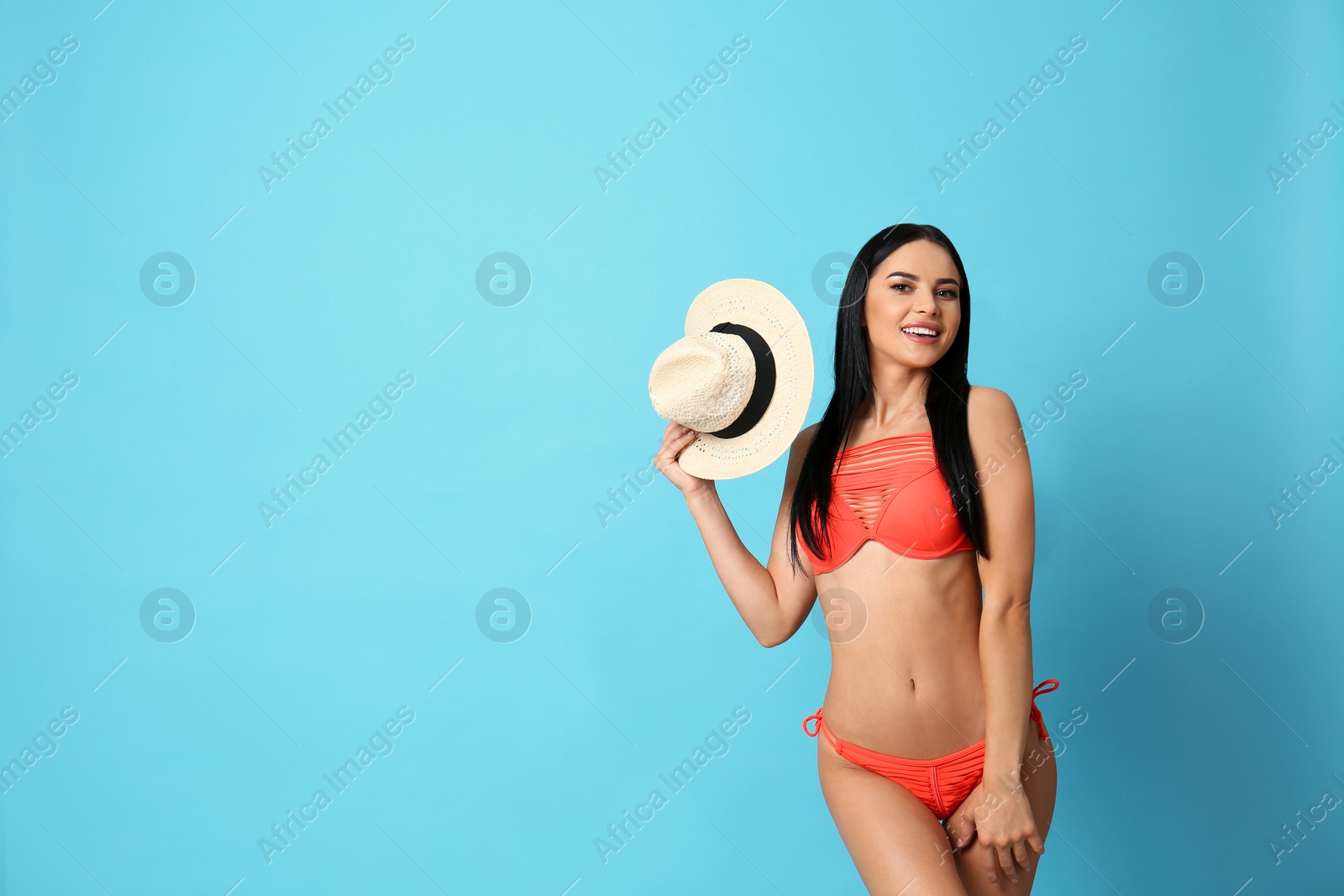 Photo of Beautiful young woman in stylish bikini with hat on light blue background. Space for text