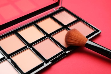 Photo of Colorful contouring palette with brush on red background, closeup. Professional cosmetic product
