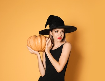 Photo of Beautiful woman wearing witch costume with pumpkin for Halloween party on yellow background, space for text