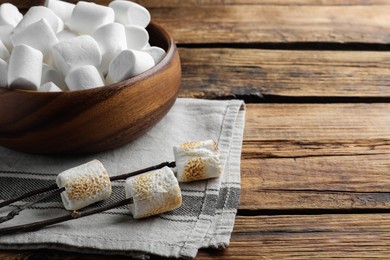 Photo of Sticks with roasted marshmallows on wooden table. Space for text