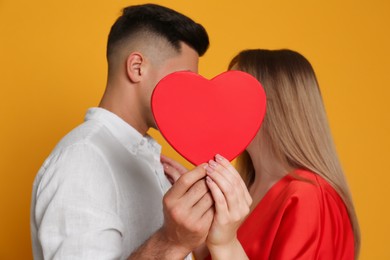 Photo of Lovely couple kissing behind decorative heart on yellow background. Valentine's day celebration