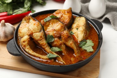 Photo of Tasty fish curry and ingredients on white table, closeup. Indian cuisine