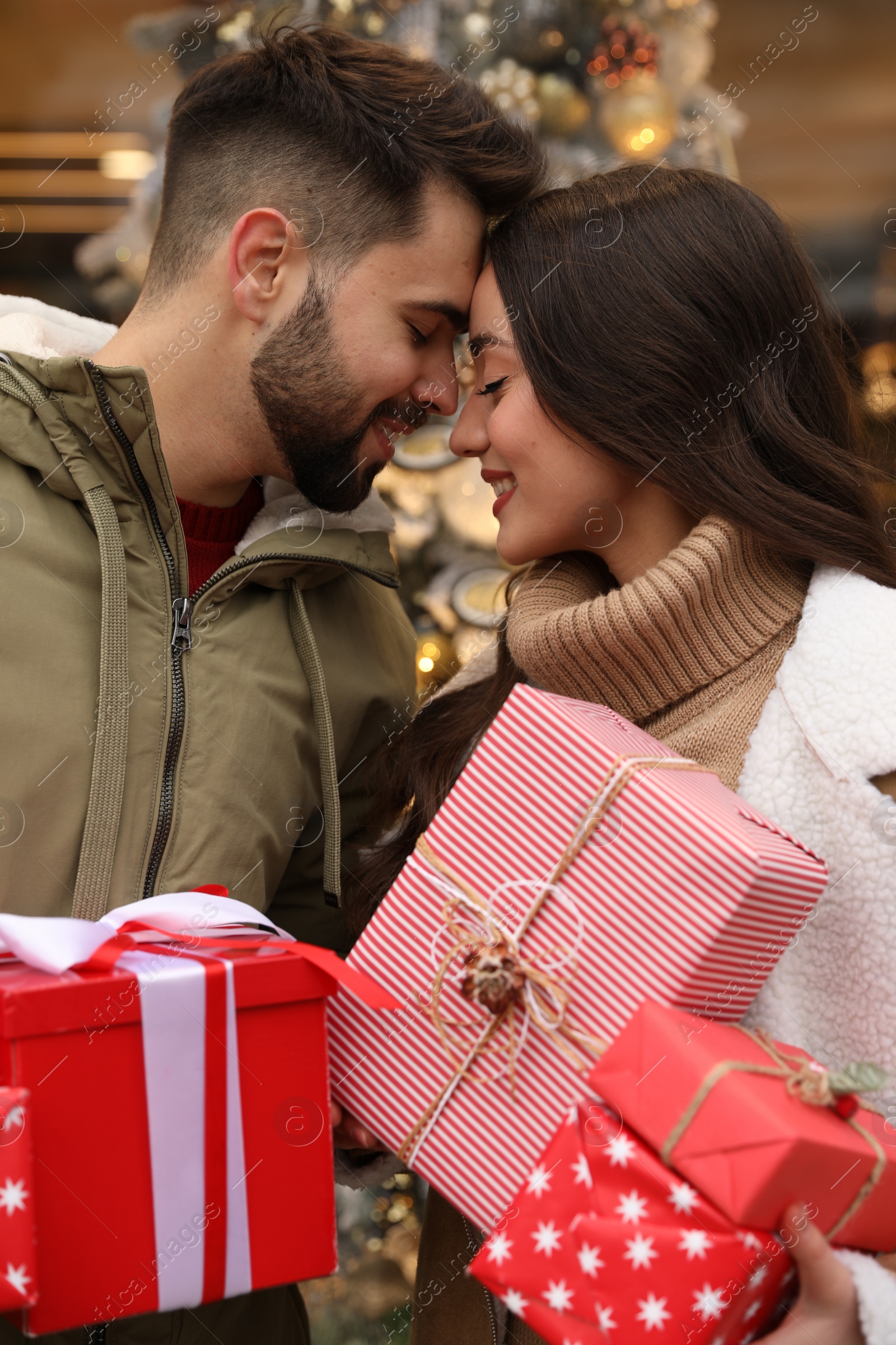 Photo of Lovely couple with Christmas presents near festively decorated store outdoors