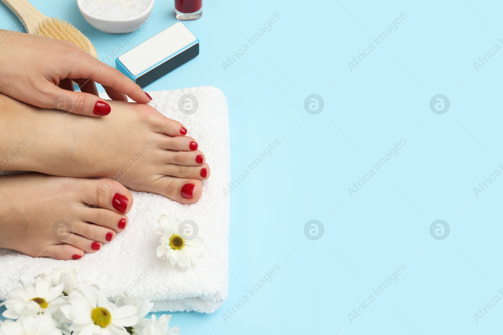 Photo of Woman with stylish red toenails after pedicure procedure and chamomile flowers on light blue background, top view. Space for text