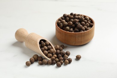 Photo of Dry allspice berries (Jamaica pepper) in bowl and scoop on white marble table