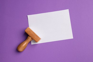 Photo of One wooden stamp tool and sheet of paper on purple background, top view. Space for text