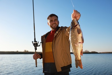 Photo of Fisherman holding fishing rod and catch at riverside