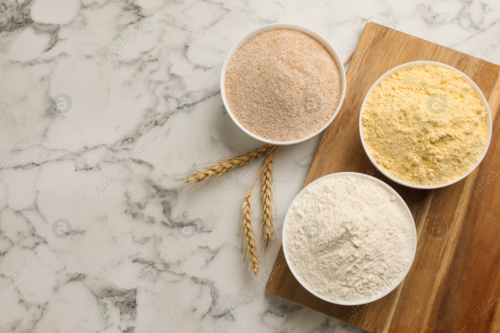 Photo of Different types of flours and wheat ears on white marble table, flat lay. Space for text