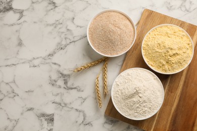 Different types of flours and wheat ears on white marble table, flat lay. Space for text