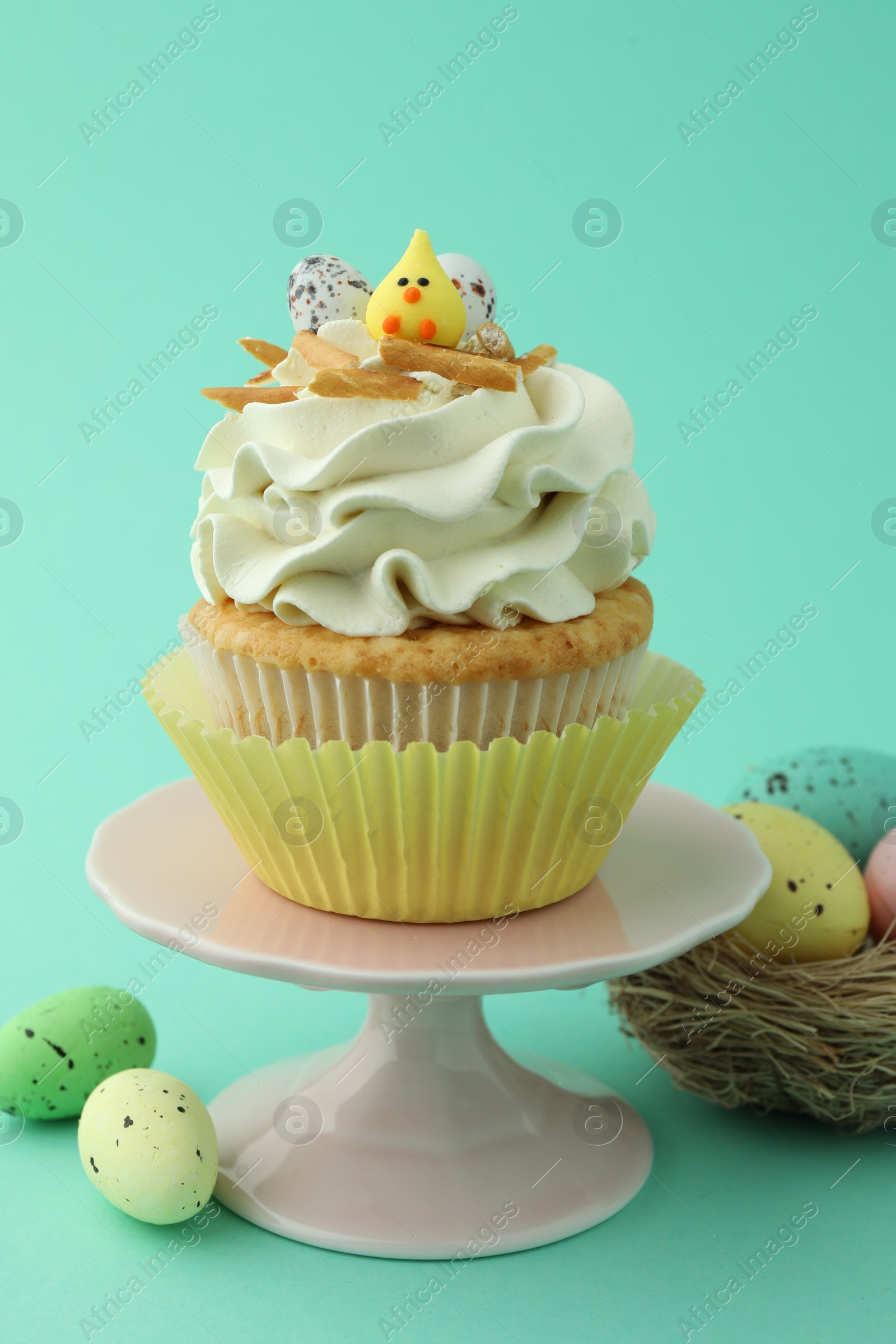 Photo of Tasty Easter cupcake with vanilla cream and festive decor on turquoise background