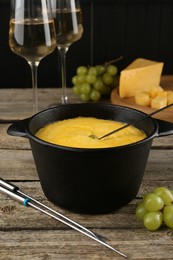 Photo of Fondue pot with melted cheese, glasses of wine and different products on wooden table