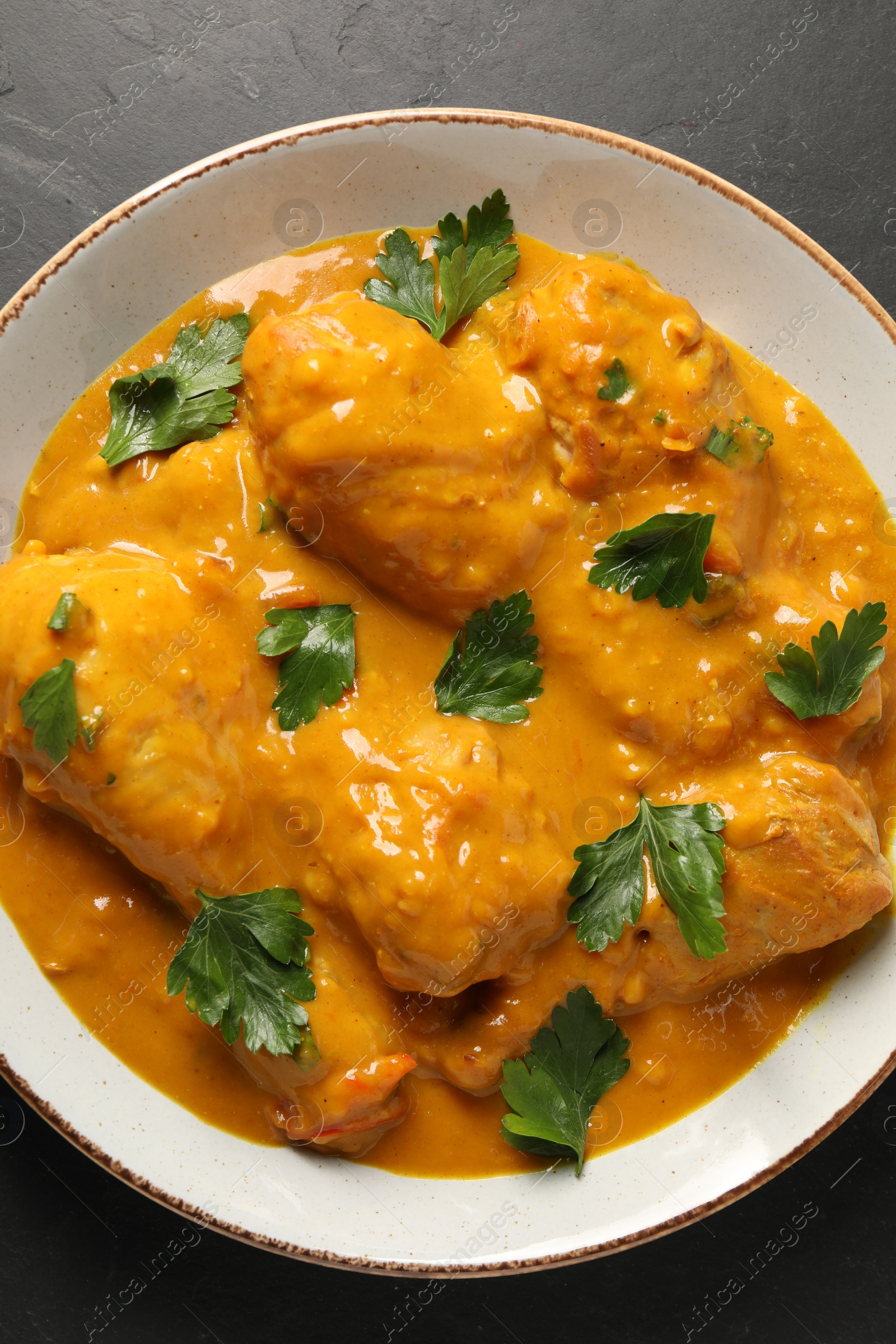 Photo of Tasty chicken curry with parsley on black textured table, top view