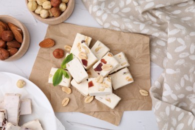 Photo of Pieces of delicious nutty nougat, hazelnuts and almonds on white table, flat lay