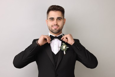 Handsome young groom with boutonniere on light grey background. Wedding accessory