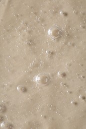 Photo of Clear cosmetic serum on beige background, macro view