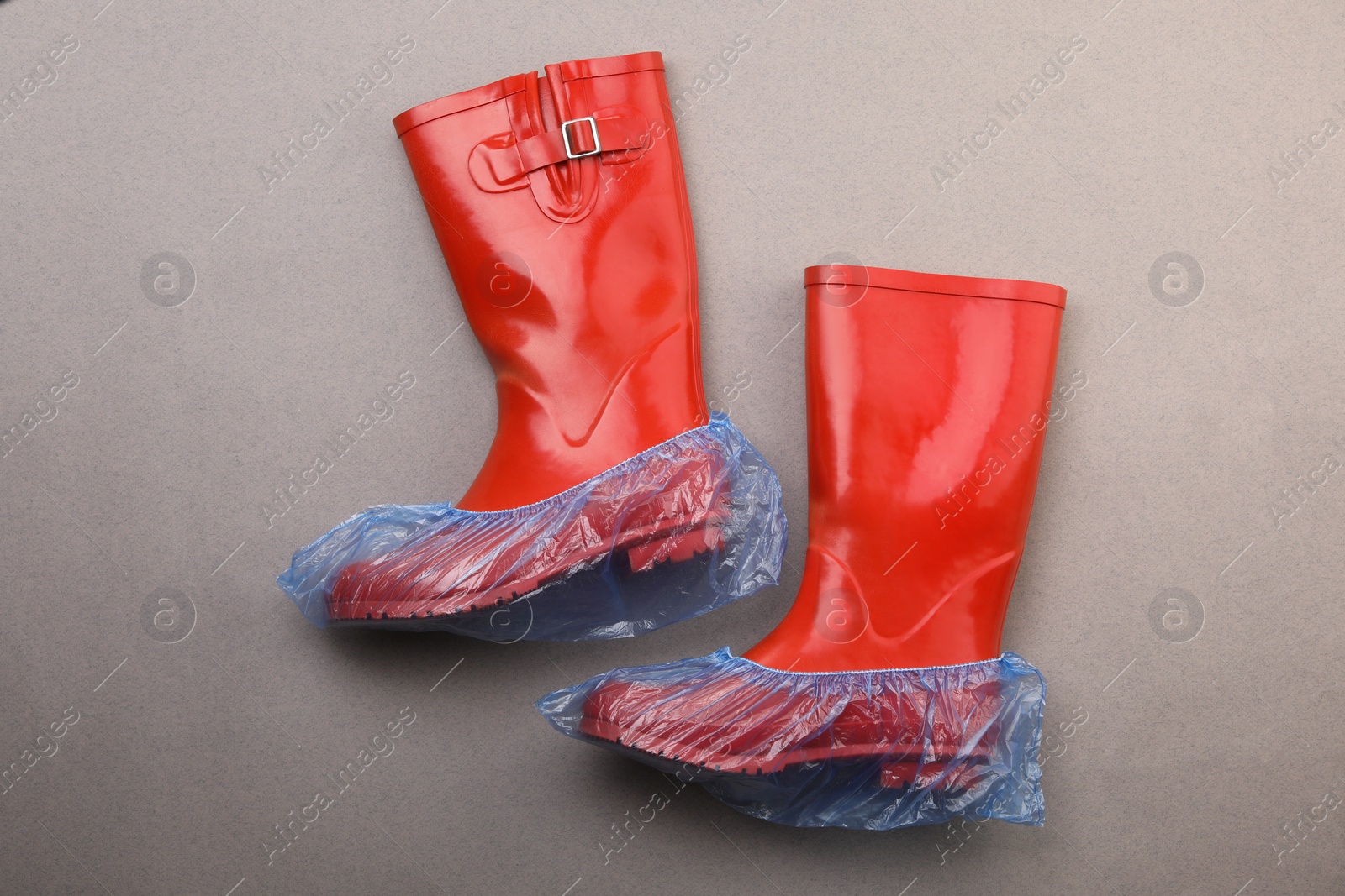 Photo of Rubber boots in shoe covers on grey background, top view