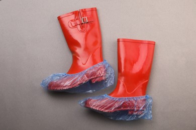 Rubber boots in shoe covers on grey background, top view