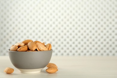Photo of Ceramic bowl with almonds on white wooden table, space for text. Cooking utensil