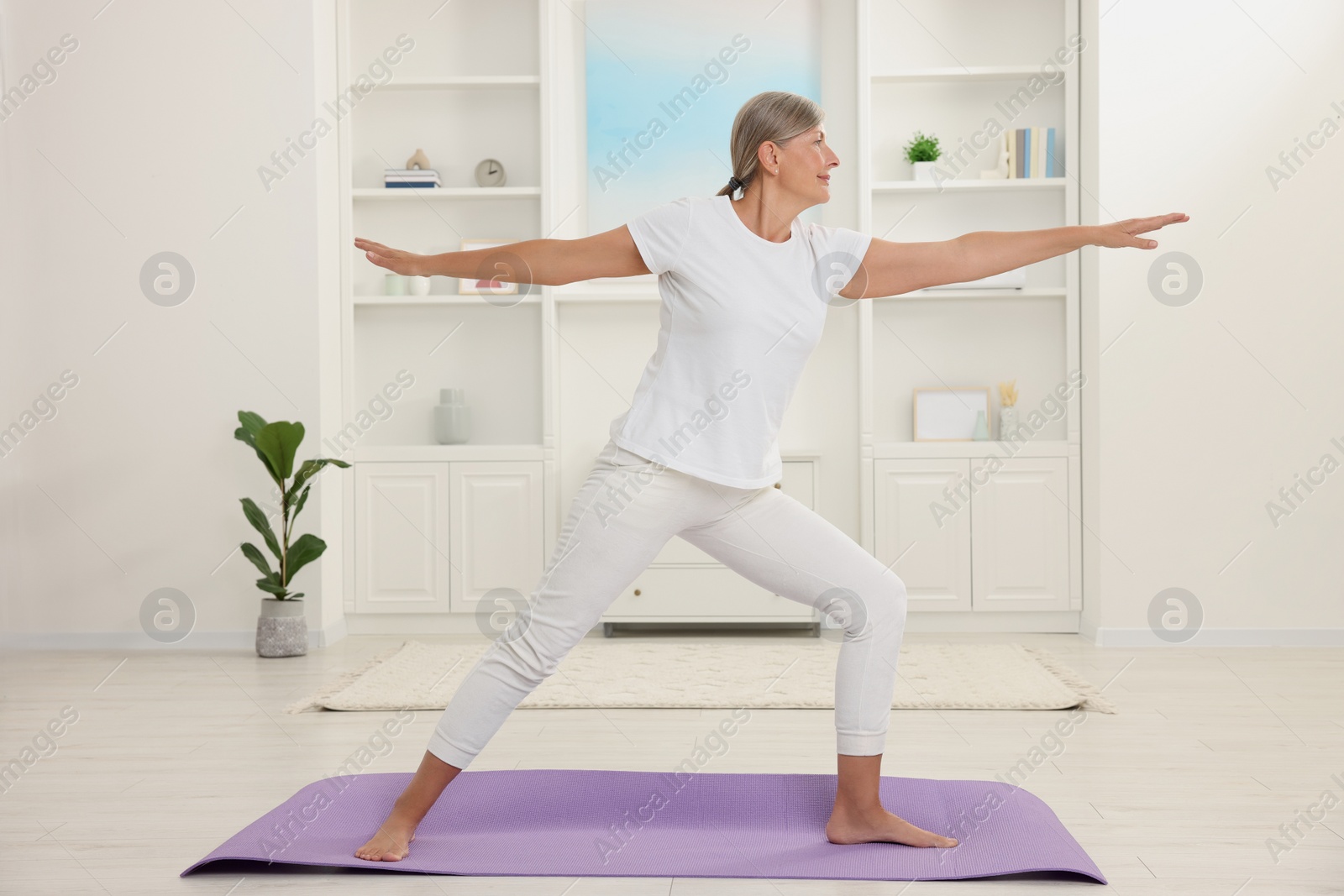 Photo of Senior woman practicing yoga on mat at home