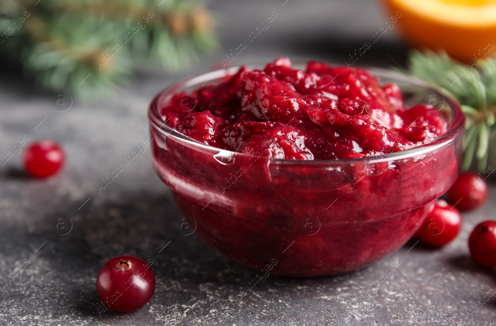 Photo of Glass bowl with tasty cranberry sauce on table, closeup