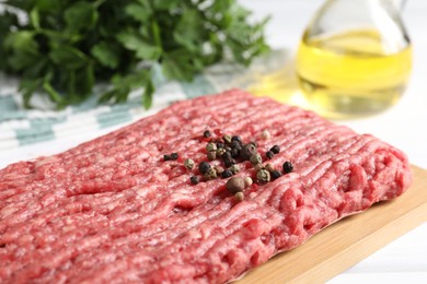 Raw ground meat and peppercorns on table, closeup