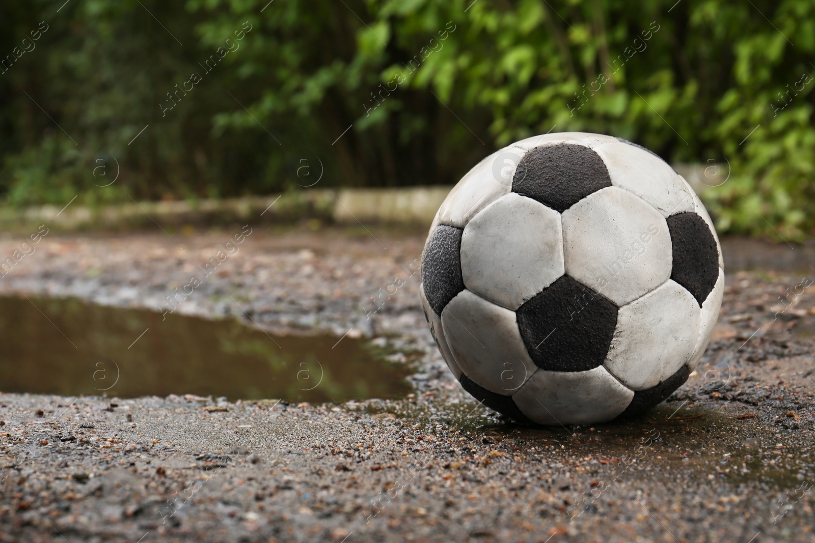 Photo of Dirty soccer ball near puddle on ground, space for text