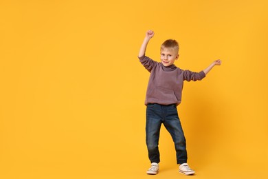 Happy little boy dancing on yellow background. Space for text