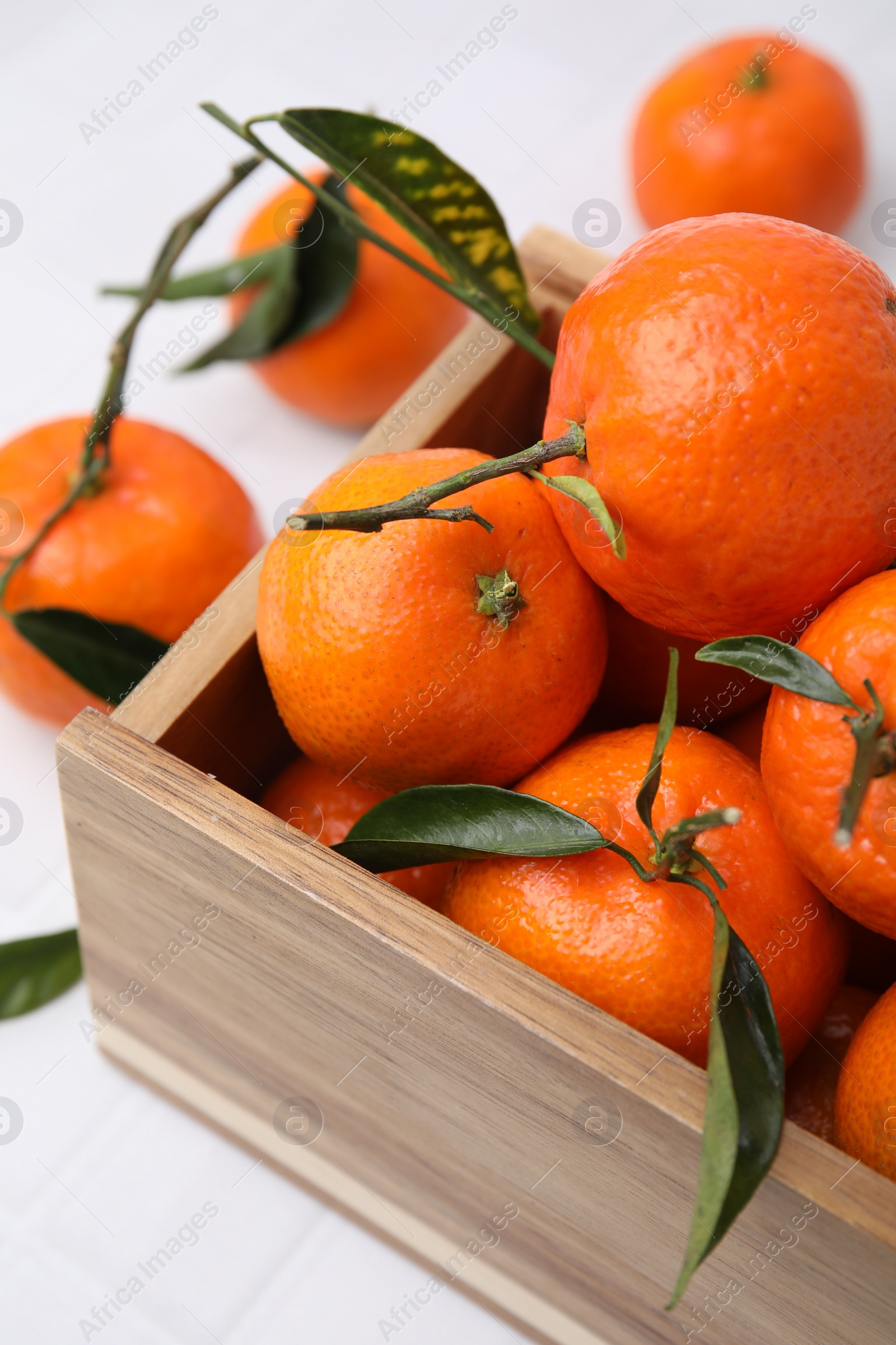 Photo of Wooden crate with fresh ripe tangerines and leaves on white table, closeup