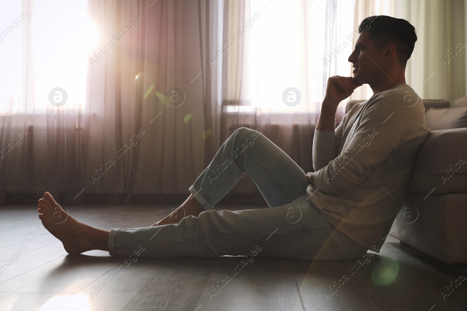 Photo of Man sitting on warm floor in living room. Heating system