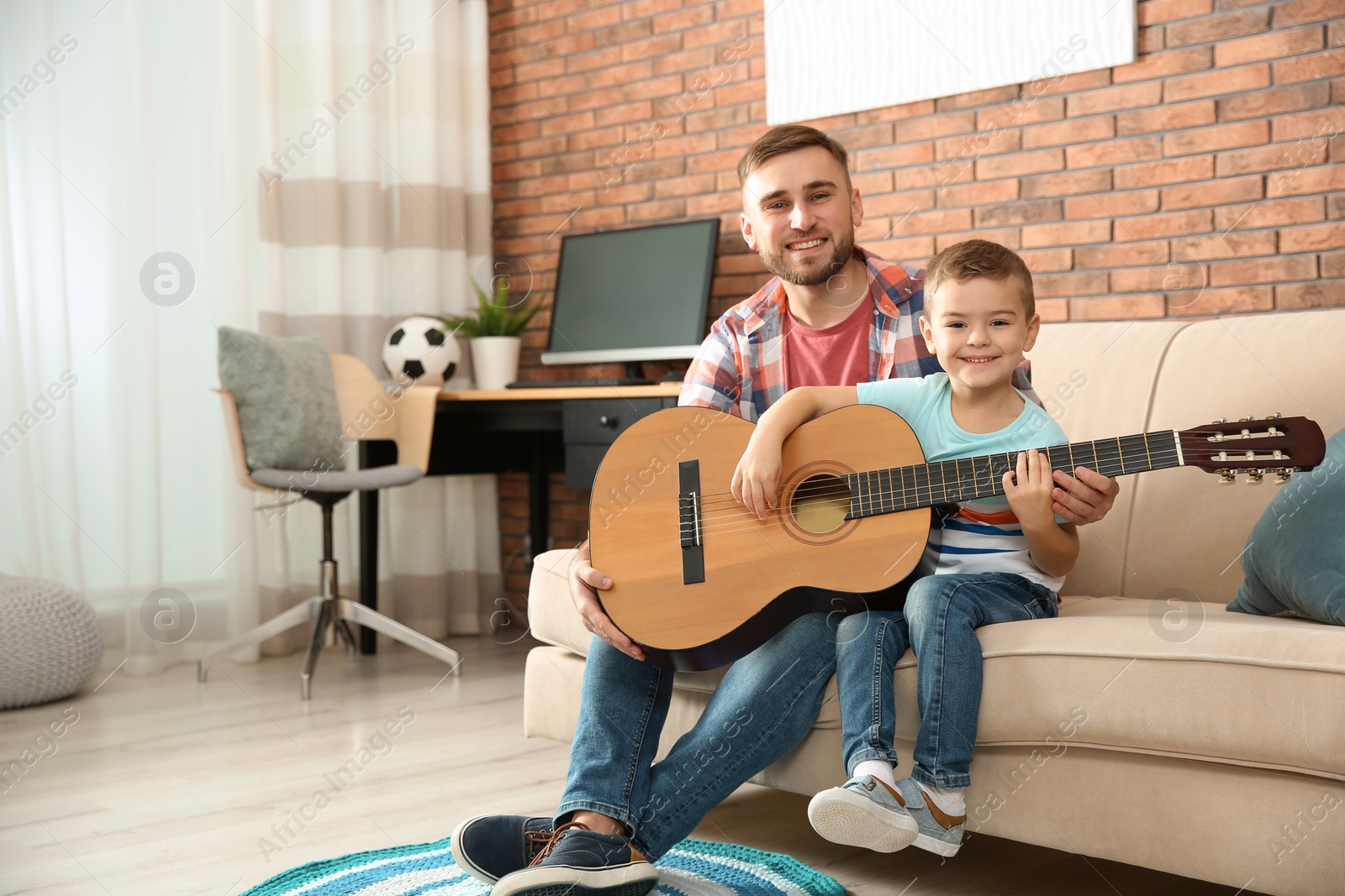 Photo of Father teaching his little son to play guitar at home