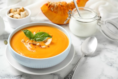 Photo of Delicious pumpkin soup in bowl on marble table