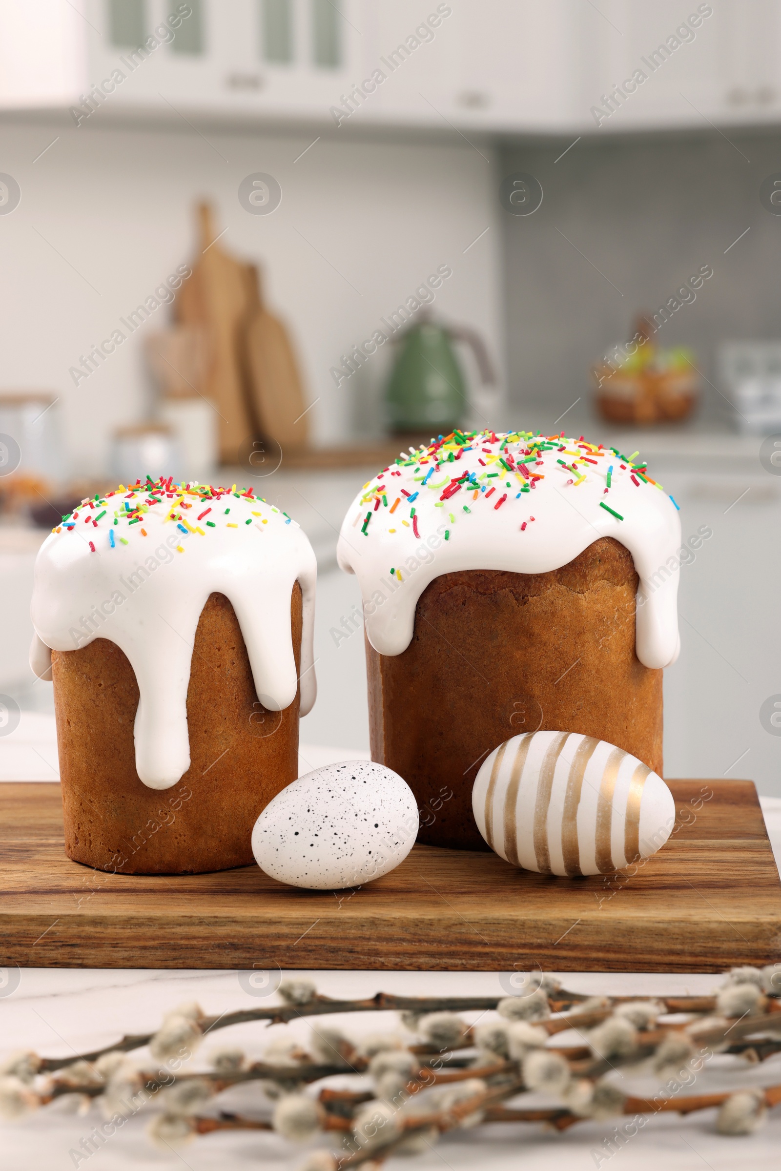 Photo of Delicious Easter cakes with sprinkles, decorated eggs and willow branches on white table in kitchen