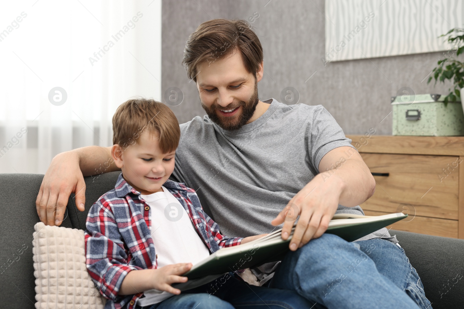 Photo of Happy dad and son reading book together on sofa at home