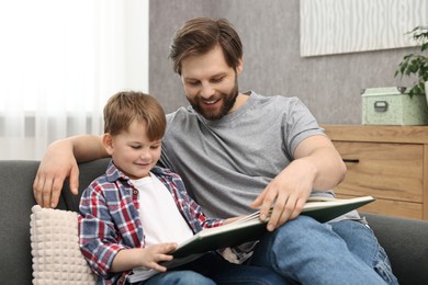 Happy dad and son reading book together on sofa at home