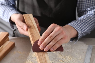 Man polishing wooden plank with sandpaper at grey table, closeup