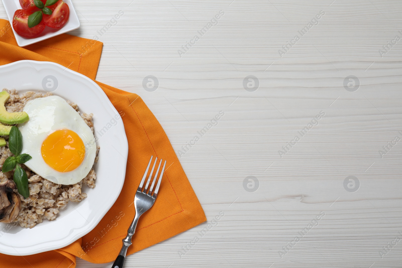 Photo of Tasty boiled oatmeal with fried egg, avocado and mushrooms served on white wooden table, flat lay . Space for text