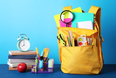 Photo of Yellow backpack and different school stationery on blue wooden table