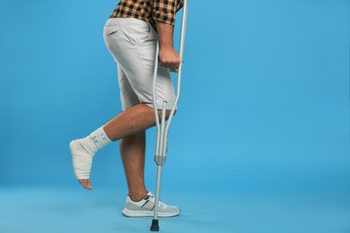 Photo of Young man with injured leg using axillary crutches on light blue background, closeup. Space for text