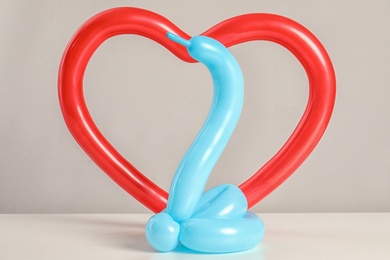 Photo of Snake and heart figures made of modelling balloons on table color light background