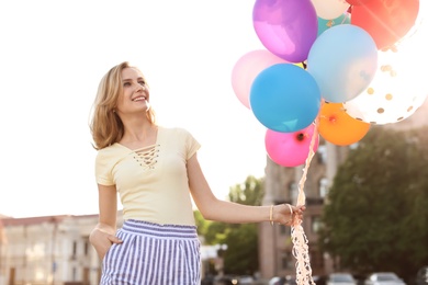 Young woman with colorful balloons outdoors on sunny day