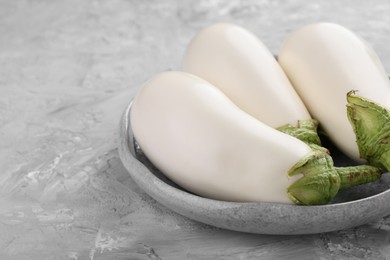 Photo of Fresh white eggplants in bowl on grey textured table, closeup. Space for text