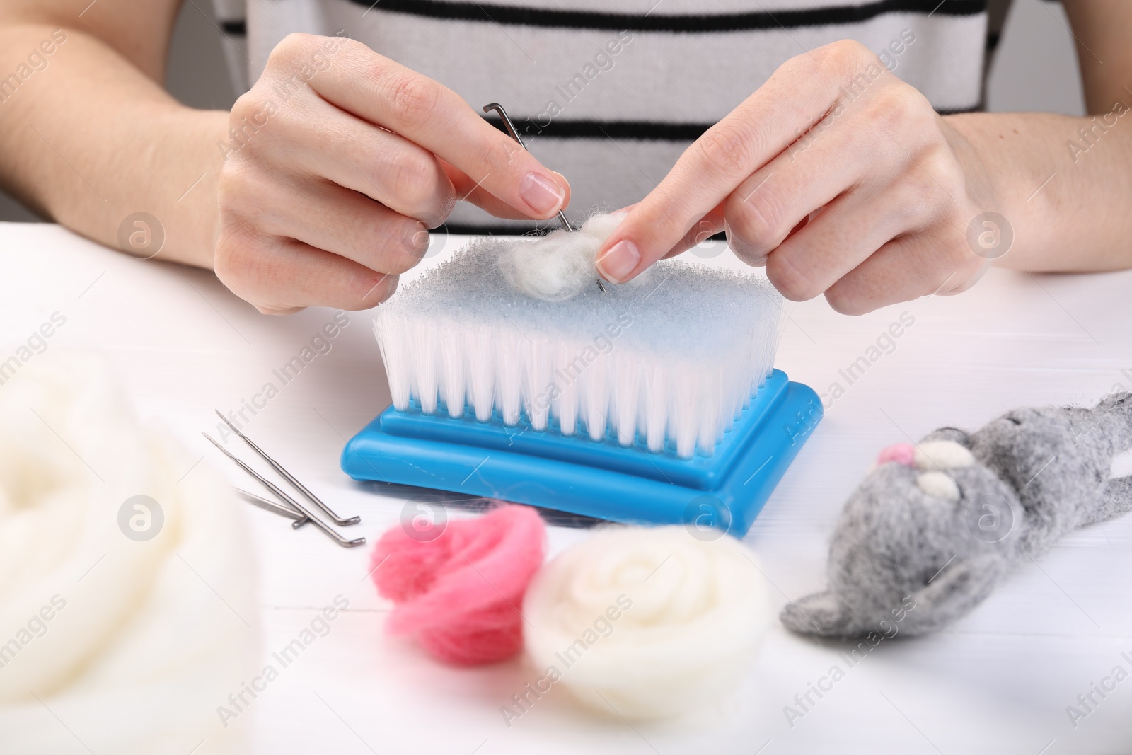 Photo of Woman felting toy from wool at white wooden table, closeup