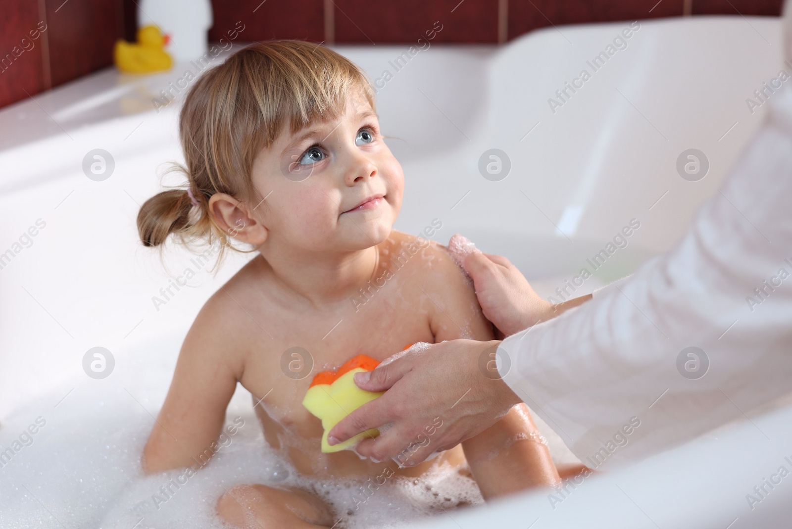 Photo of Mother washing her little daughter with sponge in bathtub, closeup