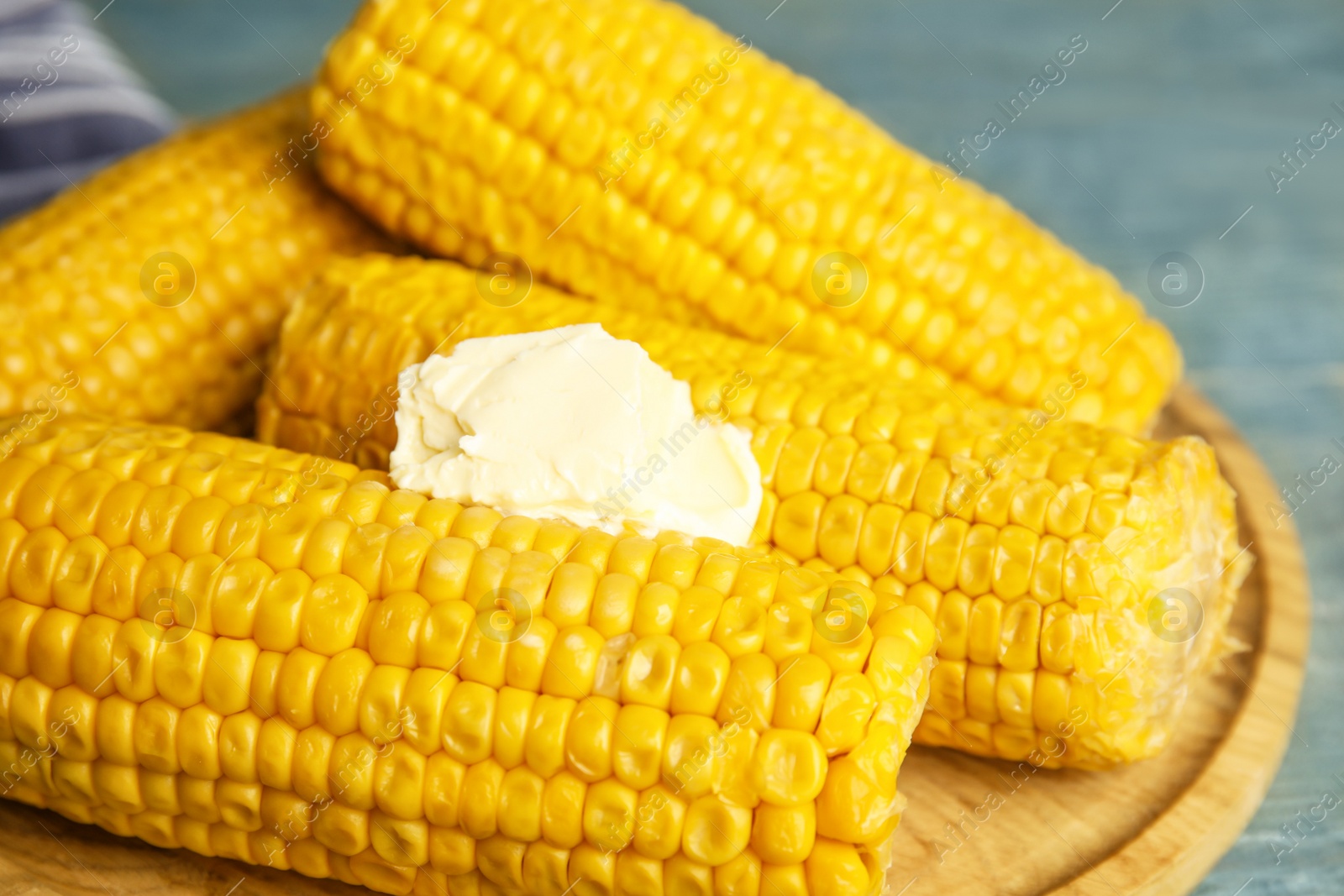 Photo of Delicious boiled corn with butter on wooden board, closeup