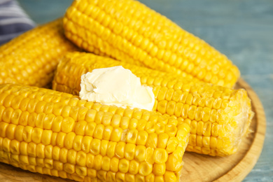 Photo of Delicious boiled corn with butter on wooden board, closeup