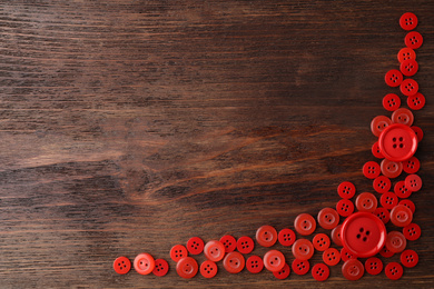 Many red sewing buttons on wooden background, flat lay. Space for text