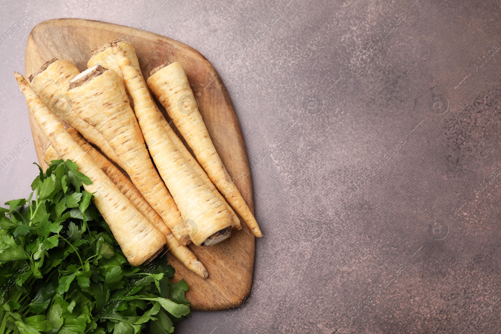 Photo of Whole raw parsley roots and bunch of fresh herb on brown table, flat lay. Space for text