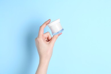 Photo of Woman holding jar of cream on light blue background, closeup. Space for text